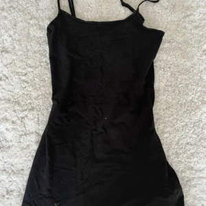 Svart kortklänning från HM Divided - Säljer en svart, tight kortklänning från HM Divided med smala axelband och enkel design. Perfekt för dig som gillar minimalistisk stil. Klänningen har en figurnära passform och är tillverkad i ett mjukt material. Som ett långt linne, storlek XS