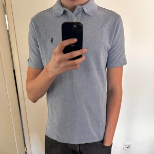 Ljusblå pikétröja från Ralph Lauren - Säljer en klassisk ljusblå pikétröja från Ralph Lauren med korta ärmar och krage. Tröjan har den ikoniska broderade loggan på bröstet och är tillverkad i mjuk bomull. Perfekt för en avslappnad och stilren look.