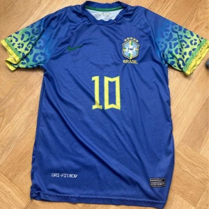 Blå Brasilien fotbollströja Neymar JR 10 - Säljer en blå Brasilien fotbollströja från Nike med Neymar JR och nummer 10. Tröjan har korta ärmar med blå och gröna leopardmönster, gula detaljer och Brasil-logga på bröstet. Perfekt för fotbollsfans! Priset kan vi diskutera 