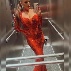 Röd glittrig långklänning/ balklänning - Säljer en superglittrig röd långklänning med figurnära passform och långa ärmar. Klänningen har en djup v-ringning och en matchande choker runt halsen. Perfekt för att sticka ut på festen eller bal. Storlek S. Köparen står för frakten 