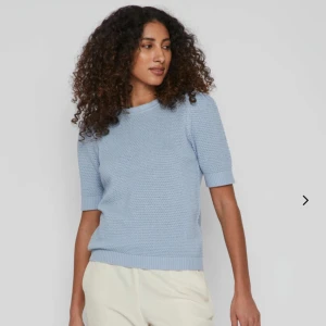 Ljusblå stickad tröja från VILA - Jättefin ljusblå stickad tröja från VILA med korta ärmar och rund halsringning. Tröjan har en fin strukturstickning och ribbade muddar vid ärmslut och nederkant. Perfekt för vår och sommar! 