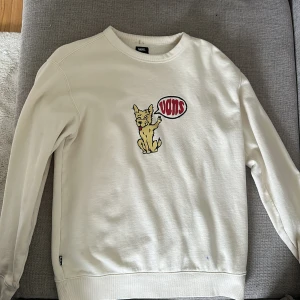 Vit sweatshirt från Vans med hund motiv  - Säljer en vit sweatshirt från Vans med ett broderat kattmotiv och texten 'Vans' på bröstet. Tröjan har rund halsringning och långa ärmar. Perfekt för dig som gillar streetwear och vill ha något unikt i garderoben.
