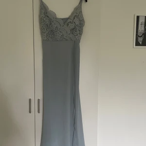 Ljusblå långklänning med spets  - Säljer en elegant ljusblå långklänning med vacker spets upptill och smala axelband. Klänningen har en figurnära passform upptill och faller rakt ner. Perfekt för bal eller festliga tillfällen.