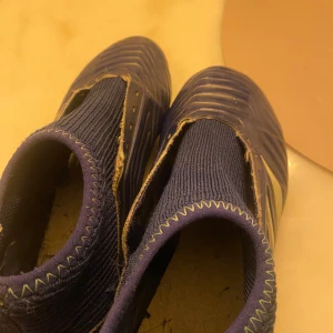 Adidas Predator fotbollsskor i blått - Säljer ett par blå Adidas Predator fotbollsskor med klassiska vita ränder på sidan och stickad ovandel. Skorna har en strumpliknande passform och gröna detaljer vid hälen. Perfekta för dig som vill dominera på planen!