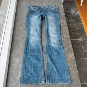 Blå bootcut vintage jeans  - Säljer ett par klassiska blå bootcut jeans med dekorativa sömmar på bakfickorna. Jeansen har låg midja och fem fickor. Aldrig använda men köpta second hand. Midjemått tvärs över 41 cm. Inebenslängd 77 cm. 