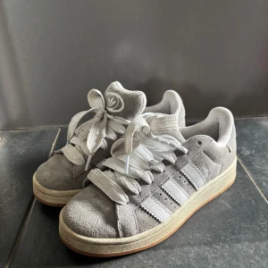 Grå Adidas Campus  - .Säljer dessa Adidas campus 00s. De är gråa med vita snören. De är använda fåtal gånger. Säljer pågrund av att de inte kommer till användning💕💕