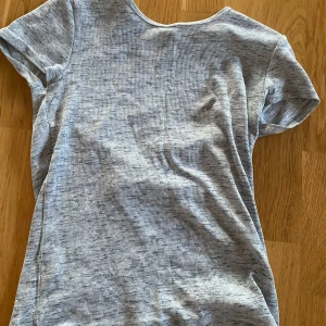 Ljusgrå ribbad t-shirt - Hej!! Min kompis säljer en ljusgrå ribbad t-shirt med korta ärmar och rund hals. Perfekt för en enkel och stilren look. T-shirten har en diskret ribbad struktur som ger lite extra detalj.