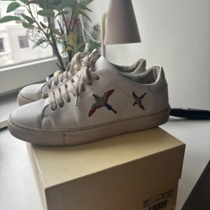 Vita sneakers från Axel Arigato med broderade fåglar - Säljer ett par vita sneakers från Axel Arigato med färgglada broderade fåglar på sidorna. Köpta på NK Göteborg för 2600kr om jag inte minns fel. Bra skick!💗