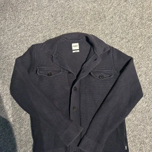 Mörkblå stickad kofta från Dobber - Säljer en mörkblå stickad kofta från Dobber i storlek small. Koftan har knappar framtill och två bröstfickor med lock. Perfekt för lager-på-lager och passar till många olika stilar.