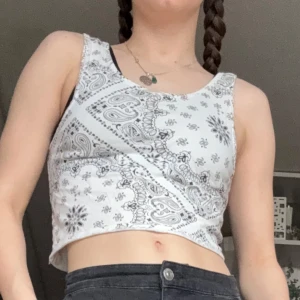 Vit croppad topp med paisleymönster - OBS!! ALLA MINA PLAGG GRATIS VID UPPHÄTMNING I RÅCKSTA!!! Säljer en vit croppad topp med svart paisley- och blommönster. Toppen är ärmlös och har rund halsringning. Perfekt för varma dagar och enkel att matcha med jeans eller shorts. Sökord linne