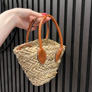 Stråväska med bruna handtag - Superfin liten handväska i flätad strå med bruna handtag och axelrem i läderimitation. Väskan har en beige tyginsida med dragsko som stängning. Perfekt för att lyfta din sommarlook! Helt slutsåld sedan många månader tillbaka 