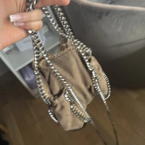 Beige axelväska från Stella McCartney - Säljer en beige axelväska från Stella McCartney med silverfärgade kedjedetaljer och rosa foder. Väskan har en mjuk form och är perfekt för dig som vill ha en snygg accessoar med plats för det viktigaste. Dustbag medföljer.
