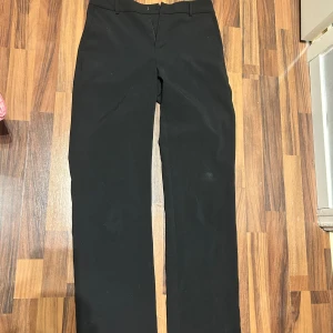 Svarta kostymbyxor från Gina Tricot - Svarta kostymbyxor från Gina Tricot med klassisk passform och raka ben. Byxorna har hällor för bälte, diskreta fickor och stängs med hake och dragkedja. Perfekta för en stilren look. Storlek 36. Inte noppriga. Använda fåtal gånger. Säljer då de är för stora för mig. 