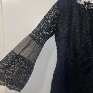 Svart spetsklänning med vida ärmar - Säljer en svart klänning i spets med vida ärmar och transparenta partier. Klänningen har rund halsringning och vacker spetsdetalj över hela plagget och djup rygg. Perfekt för dig som vill sticka ut med en elegant look. Bara använd en gång.