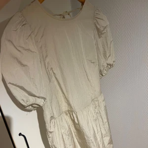 Beige klänning med puffärmar och knyt i ryggen - Säljer en beige klänning med puffiga kortärmar och rund halsringning. Klänningen har knytband i ryggen. Perfekt för vår och sommar, i ett tunt och lätt material❤️❤️