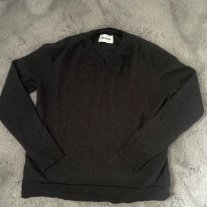 Mörkgrå ulltröja från Zadig & Voltaire - Säljer en stilren mörkgrå ulltröja från Zadig & Voltaire. Tröjan har v-ringad hals. Tröjan har ett litet hål (se bild 4) som väldigt lätt kan fixas. Tröjan är i storlek S och är lite lite kort i längden.