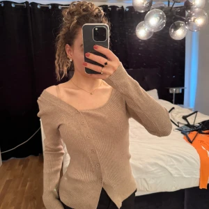  omlottkofta från Dazy - Säljer en beige ribbad omlottkofta från Dazy med asymmetrisk knäppning och lång ärm. Tröjan har en unik offshoulder-design och är perfekt för dig som gillar trendiga detaljer och mjuka material.