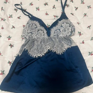 Mörkblå satin linnetopp med spets - Säljer en mörkblå linnetopp i satin med tunna axelband och vacker vit spetsdetalj 