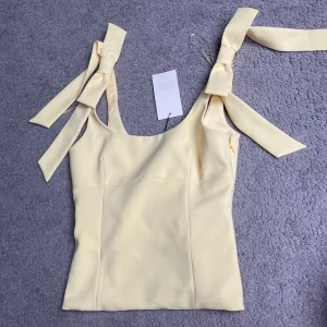 Ljusgul topp med rosetter från ZARA - Supersöt ljusgul topp från ZARA med breda axelband som knyts i rosetter. Helt ny men tyvärr förstor för mig 😭❤️tryck gärna på köp nu knappen ❤️