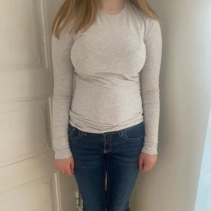 Ljusgrå långärmad topp - En enkel och stilren ljusgrå långärmad topp i mjukt material. Modellen är tight och passar perfekt till jeans eller kjol. Klassisk rund halsringning och utan synliga detaljer eller mönster.
