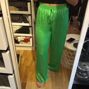Gröna vida byxor med dragsko - Säljer ett par gröna, vida byxor med dragsko i midjan. Byxorna har en glansig finish och är perfekta för dig som gillar en avslappnad men ändå trendig look.