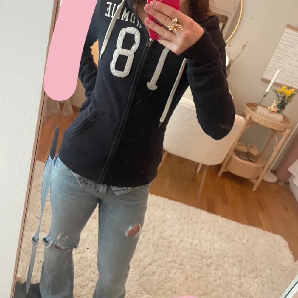 Mysig marinblå hoodiejacka från Abercrombie & Fitch med dragkedja framtill och vit text på bröstet. Jackan har huva med dragsko och två fickor framtill. Perfekt för en avslappnad stil. Skriv om fler bilder, frågor eller diskussion om priset!🤗💗IGNORERA SISTA BILDEN TOG BARA DEN FÖR ATT MAN SET PASSFORMEN!. Hupparit & Collegepaidat.
