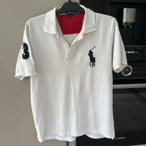 Polo Ralph Lauren Vit piké - Vit pikétröja från Polo Ralph Lauren med klassisk krage och knappar. Stor broderad logga på bröstet och en stor siffra 3 på ärmen. Röd insida vid kragen och custom fit-modell. Man får 5% RABATT när följer NordqvistFashionCloset på Instagram samt här på plick!!😊Mvh Wilgot