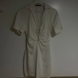 Vit kort klänning med knyt från Zara - Säljer en vit kort klänning från Zara med v-ringning och knyt framtill. 