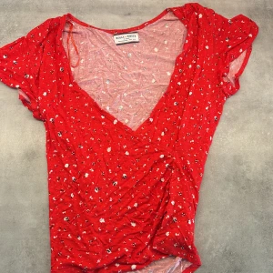 Röd blommig omlottklänning från Holly & Whyte - Supersöt röd omlottklänning från Holly & Whyte med små vita och blå blommor. Klänningen har korta ärmar, v-ringning och lätt rynkade detaljer i midjan. Perfekt för sommarens alla tillfällen!❣️❣️Storlek S!!❣️❣️