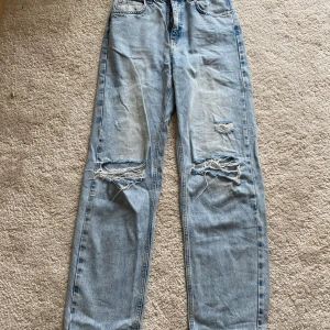 Ljusblå jeans med slitningar från Gina Tricot - Ljusblå jeans från Gina tricot young med raka ben och tydliga slitningar över knäna. Klassisk femficksmodell med dragkedja och knapp framtill. Har haft byxorna länge men inte använt mycket.