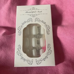 Vita lösnaglar i ask Beautiful Nail - Säljer ett set med vita lösnaglar i klassisk fyrkantig form från Beautiful Nail. Naglarna kommer i en elegant vit ask med dekorativa detaljer och ett fönster som visar naglarna. Perfekt för dig som vill fixa snygga naglar snabbt hemma.