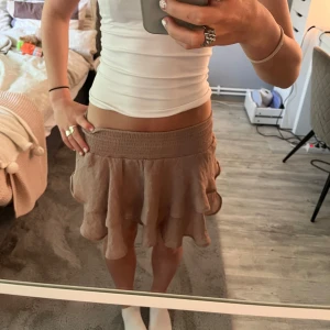 Beige volangkjol med resårmidja - Supersöt beige kortkjol med volanger och bred resår i midjan. Kjolen har en flowy och luftig känsla, perfekt för varma dagar. Enkel att matcha med crop tops eller stickade tröjor.
