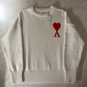 Ami tröja   - En vit stickad tröja med ett rött hjärta på vänster sida  som är broderat. en perfekt tröja på sena sommarkvällar där den håller dig varm och även bra i kyliga dagar. Tröjan är i storlek xl men jag skulle säga tröjan är i mindre storleken och passar en person som bär L väldigt bra där jag själv bär storleken L och den sitter perfekt