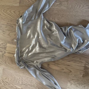 Glittrig silverbody från H&M - Snygg kort glittrig body från H&M i metallic silver. Klänningen har lång ärm, v-ringning och markerad midja med rynkade detaljer. Perfekt för dig som vill sticka ut med en cool och trendig look.