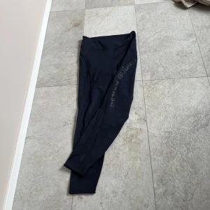 Svarta träningsbyxor från Better Bodies - Snygga svarta träningsbyxor från Better Bodies med diskret logga längs benet. De är högmidjade och tillverkade i ett stretchigt syntetmaterial som sitter tight och bekvämt. Med ett mycket diskret camouflage mönster.