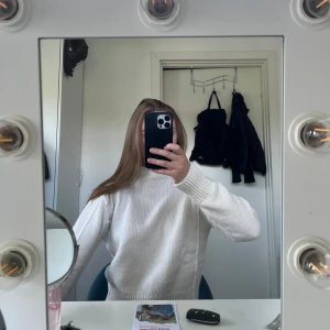 Vit stickad polotröja - Säljer en vit stickad polotröja med hög hals och raka, långa ärmar. Tröjan har en ribbad kant nedtill och vid ärmsluten. Helt ny aldrig använd