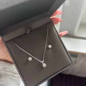 Silverset med halsband & örhängen Albrekts Guld - Snyggt smyckeset från Albrekts Guld i äkta silver med halsband och matchande örhängen. Båda har glittrande kubisk zirkonia i blomformad design som ger en elegant och fräsch look. Kedjan är tunn och stilren, perfekt för att lyfta din outfit.