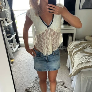 Vit spetsblus från French Pastry - Supersöt vit blus i spets från French Pastry med v-ringning och svarta spetsdetaljer längs kanten. Blusen är genomskinlig, har korta ärmar och en flowy, feminin passform som ger en romantisk vibe. Perfekt för dig som gillar vintageinspirerad stil.