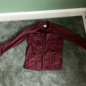 Vinröd overshirt från John Henric - Snygg vinröd overshirt från John Henric i 100% bomull. Jackan har klassisk krage, knäppning framtill och flera fickor med lock. Perfekt att slänga över en t-shirt för en chill och stilren look.