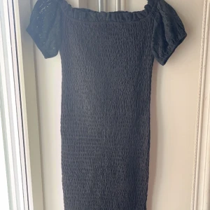 Svart kort klänning med spets från SHEIN - Supersöt svart kort klänning från SHEIN med puffiga spetsärmar och volangkant nertill. Smockad över hela kroppen för en tight passform och offshoulder-modell. Perfekt för dig som gillar romantiska detaljer och vill sticka ut lite extra.