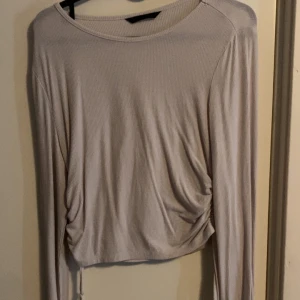 Beige ribbad långärmad topp - Säljer en vit ribbad långärmad topp med snörning i sidan. Croppad modell med lätt rynkade detaljer som ger en snygg passform. Står inte vilken storlek men skulle gissa S/M