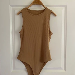 Beige ribbad ärmlös bodysuit -  beige bodysuit med ribbad struktur och rund halsringning. Ärmlös modell som sitter tight