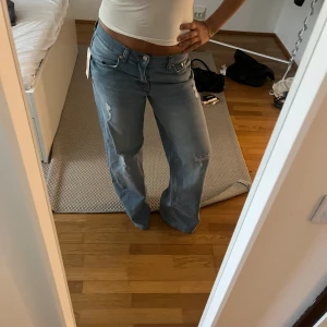 Ljusblå wide jeans med slitningar - Säljer ett par ljusblå jeans med breda ben och snygga slitningar på låren och knäna. De är helt nya och oanvända, prislappen sitter ännu på