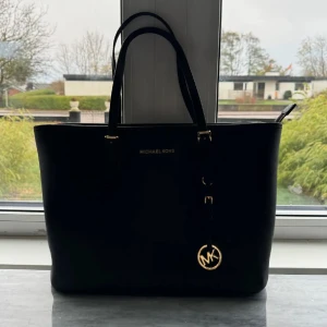 Svart Micheal Kors väska - Säljer en elegant svart handväska från Michael Kors i mycket bra skick. Väskan har en stilren design med guldiga detaljer och ett klassiskt MK-hänge.🖤 det finns små repor på hänget, kolla bild nr 3. Inget som man tänker på eller lägger märke till och syns inte tydligt från långt avstånd. Själv får jag plast med mitt cykelbatteri och skoldator i den.  Nypris: Ca 3000kr. Finns lite små vita repor på väskan, inget som är jättetydligt men skriv för fler bilder. 