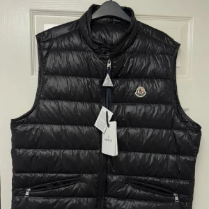 Svart gui väst från Moncler - Läs beskrivningen. Snygg svart dunväst från Moncler med quiltad design och hög krage. Västen har dragkedja framtill, två fickor med dragkedja och Moncler-logga på bröstet. Perfekt för lager-på-lager och streetstyle. Storlek 4 Obs tagsen följer inte med