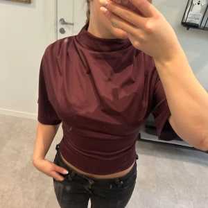 Vinröd topp - Säljer en vinröd croppad polotopp med halvlånga ärmar och hög hals. Toppen har en tight passform över midjan och har super snygga detaljer som skapar en fin siluett🥰toppen är endast använd en gång så i nyskick❤️