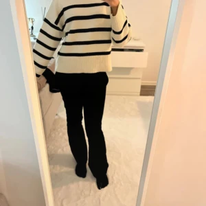 Randig stickad tröja i vitt och svart - Säljer en snygg stickad tröja med breda svarta ränder på vit botten. Tröjan har en rak, lite loose passform och långa ärmar. Perfekt för dig som gillar klassisk stil med en modern twist.