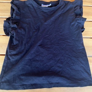 Marinblå volangärmaf topp - Supersöt mörkblå topp från Gina Tricot med volangdetaljer på ärmarna. T-shirten har rund halsringning och är tillverkad i mjuk bomull, perfekt för en chill och stilren look. Passar dig som gillar enkla men snygga detaljer. Säljer pga att jag inte tycker den passar mig jätte bra. T-ahirten är i stl 146/152 men passar mig som kan ha xxs/xs. (Andvänd fåtal gånger)