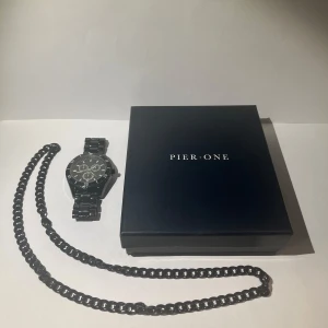 Pier One - Svart halsband och klocka  - Säljer ett stilrent svart halsband med grova länkar och en matchande svart klocka från Pier One. Klockan har metallarmband, rund urtavla och tydliga vita markeringar. Perfekt för dig som gillar en clean och modern look.