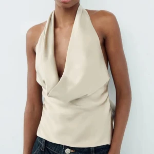 Champagnefärgad halterneck topp i satin - Säljer en champagnefärgad halterneck topp i glansig satin med djup draperad urringning och öppen rygg. Aldrig använd endast testad! 💖